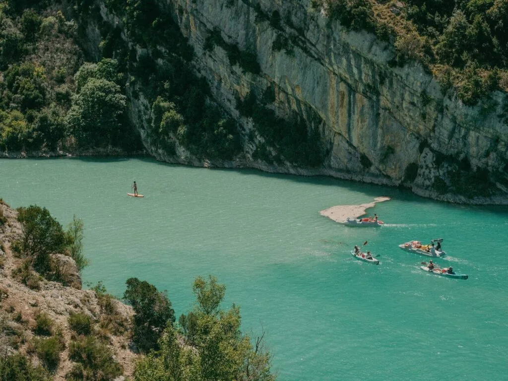 People paddleboarding and kayaking on a turquoise river by cliffs